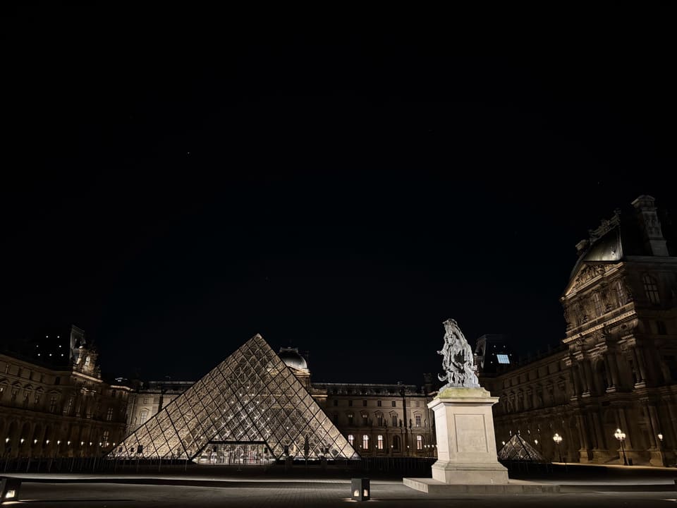 The Louvre's glass pyramid glowing at night in an empty courtyard, an equestrian statue lit against the dark sky