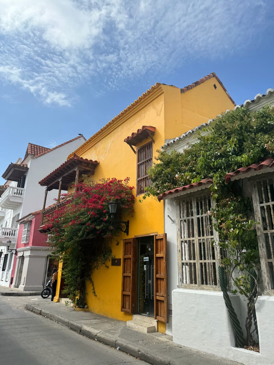 Yellow colonial house with wooden balcony draped in red bougainvillea on a sunlit Cartagena old-town street