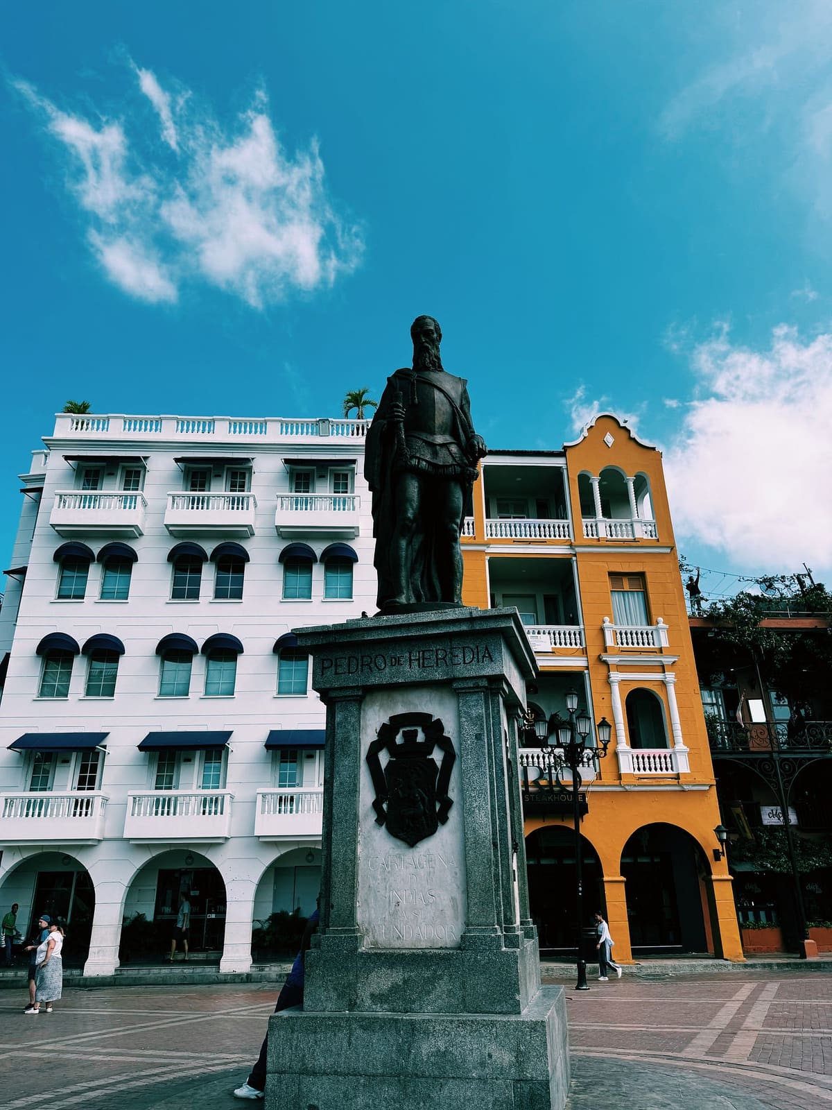 Bronze statue of Pedro de Heredia on a stone plinth in Cartagena's old town, white and saffron colonial balconies rising behind it