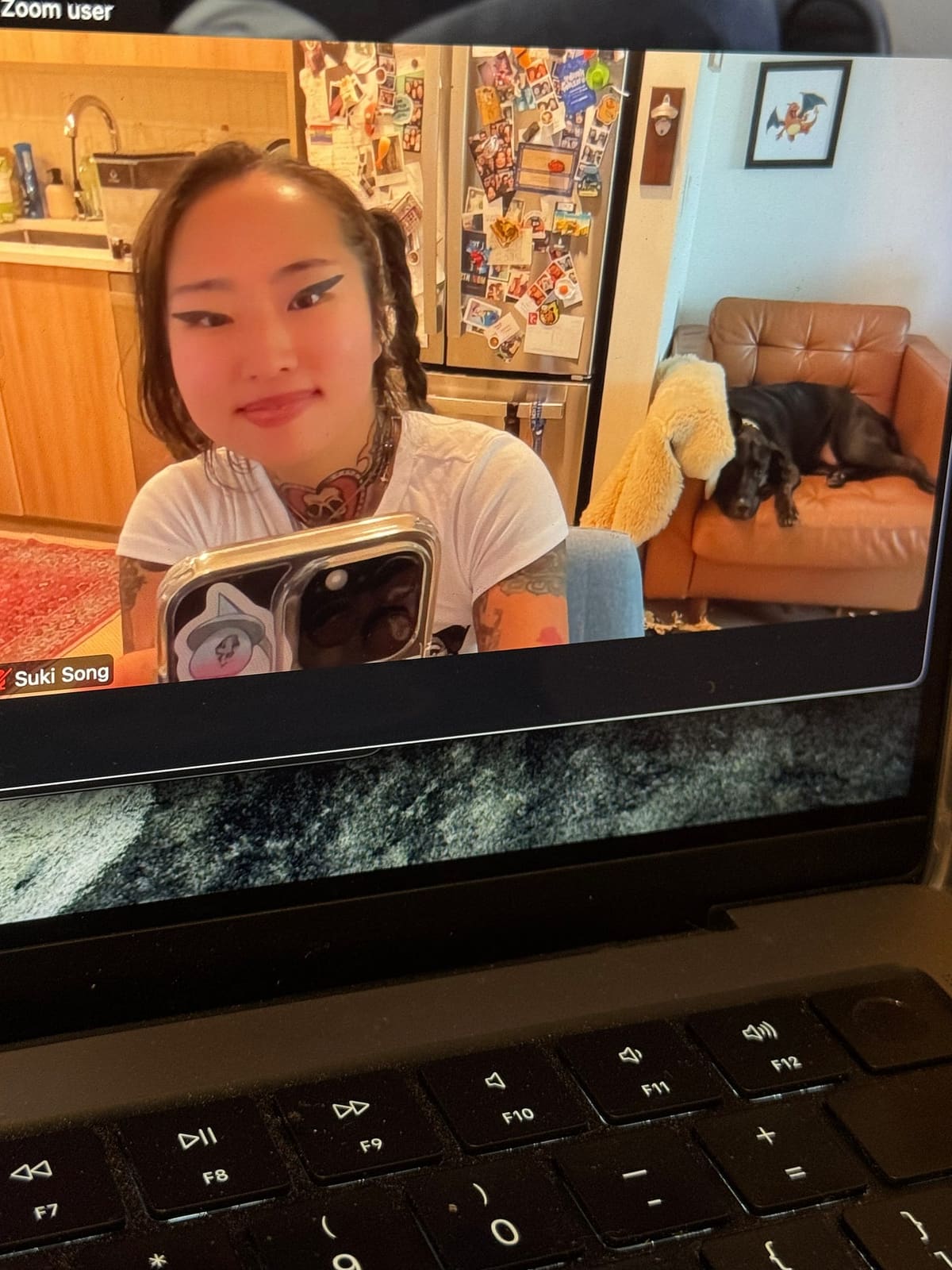 Laptop screen on a Zoom call: the author smiles holding her phone while Love, her black Lab, lounges on a chair behind her.
