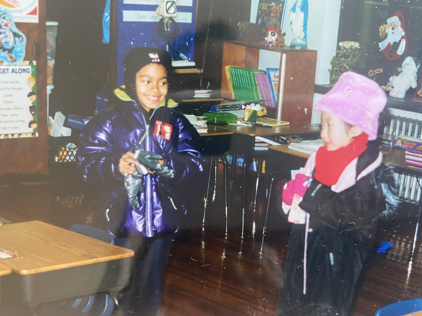 Faded childhood photo: the author as a little girl in a pink fuzzy hat and red scarf, with a classmate in a purple coat.